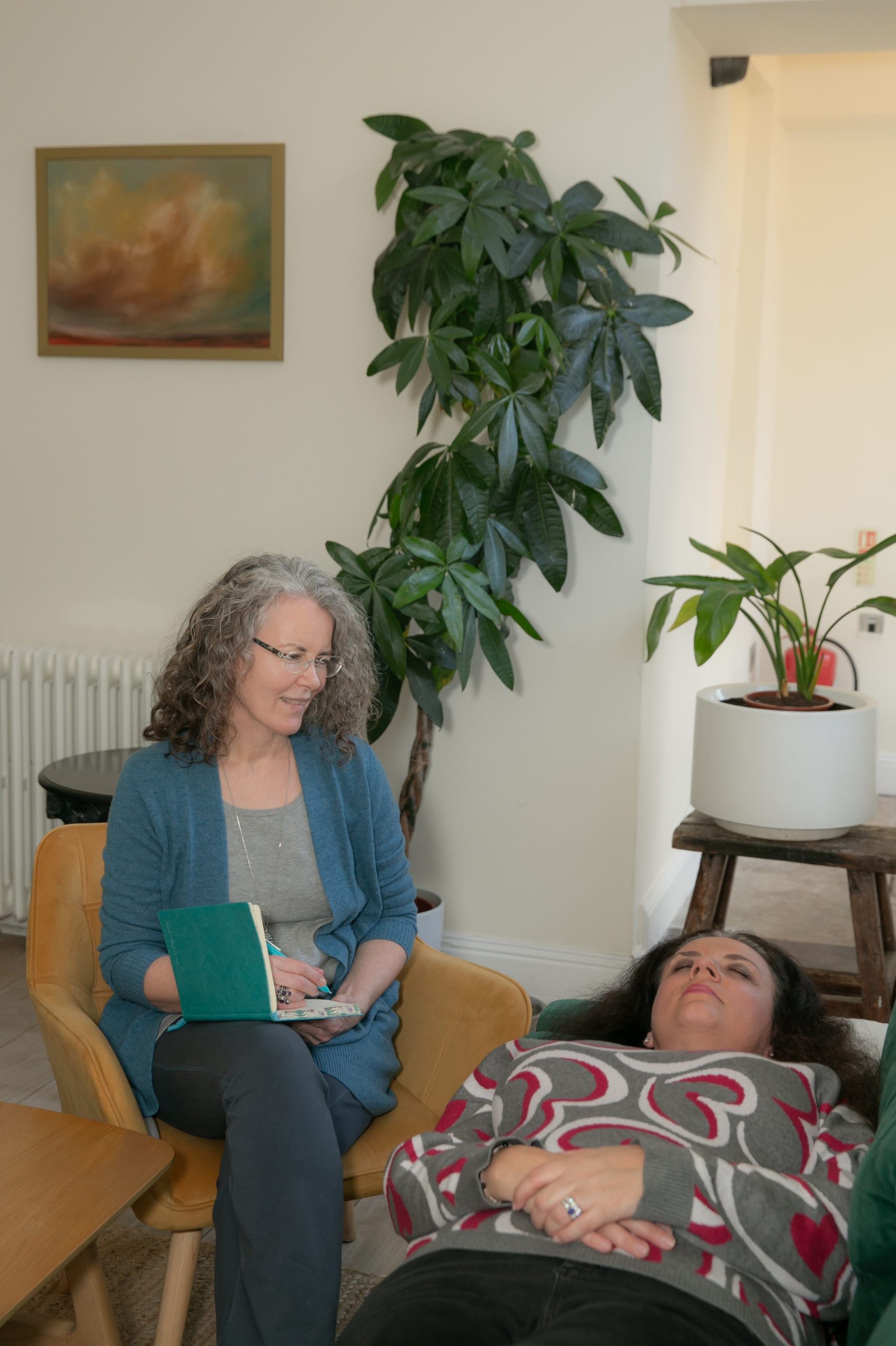 An image of me; a woman in her 50s with long, brown greying curls and rimless glasses. I am looking into the camera and smiling.